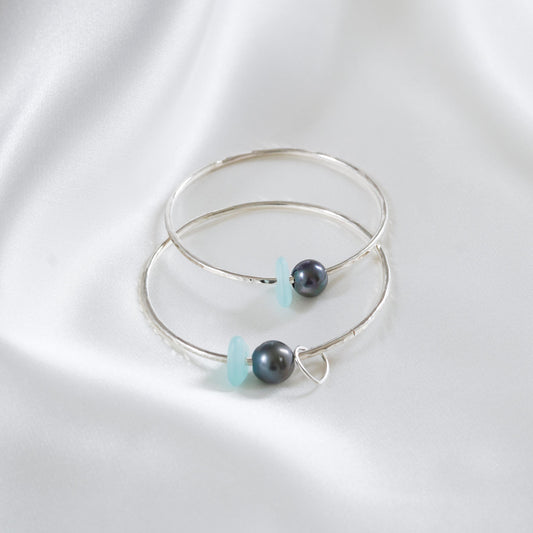 Two silver bangles with tahitian pearls and blue sea glass on a white background