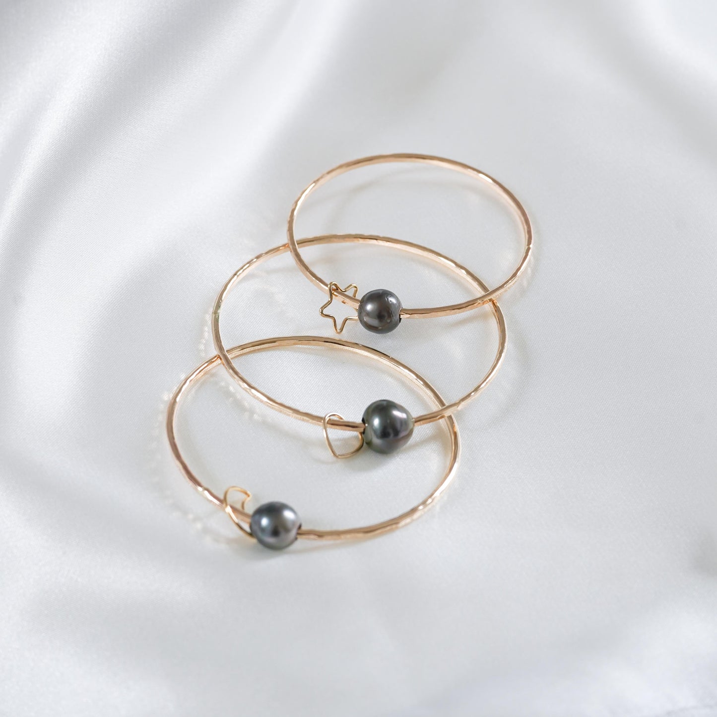 Three gold bangles with tahitian pearls and gold charms on a white background