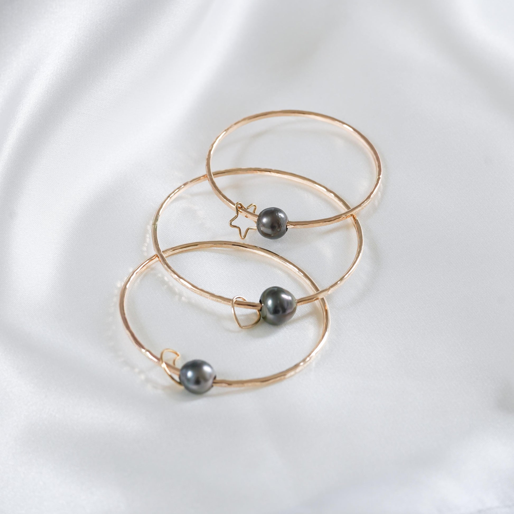 Three gold bangles with tahitian pearls and gold charms on a white background