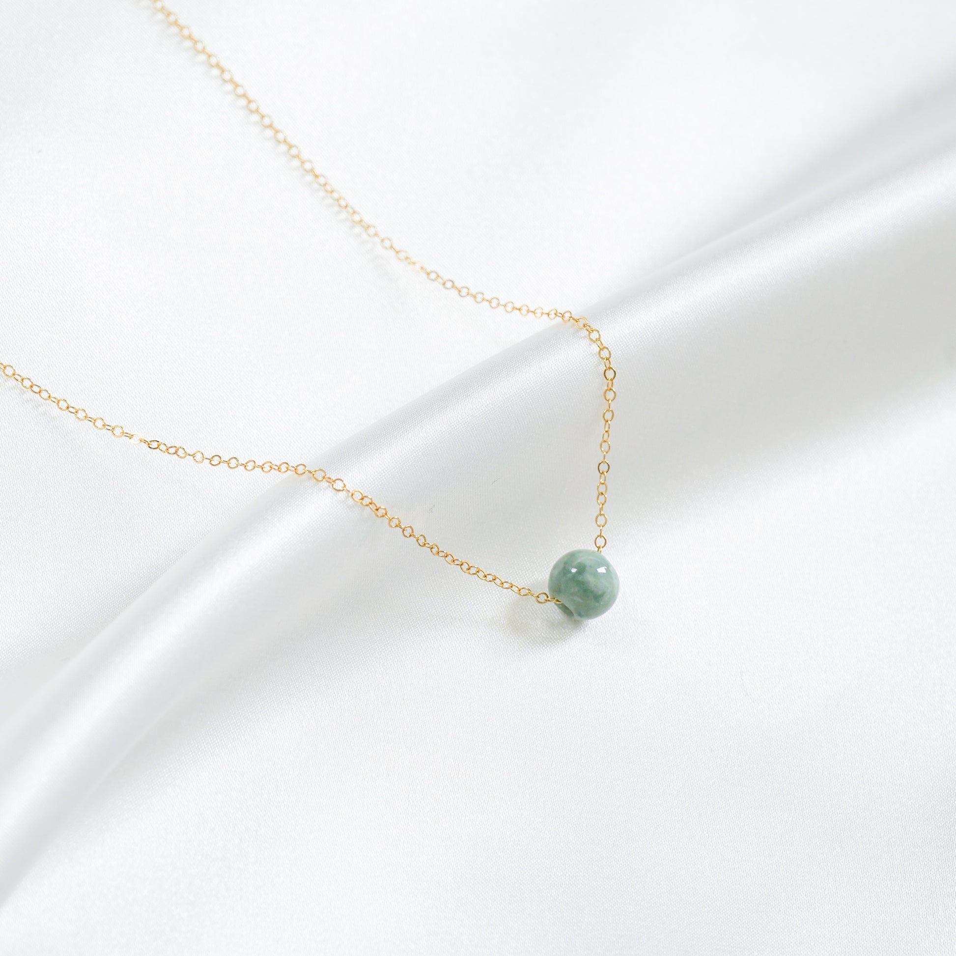 Necklace with a green round jade bead on a white background