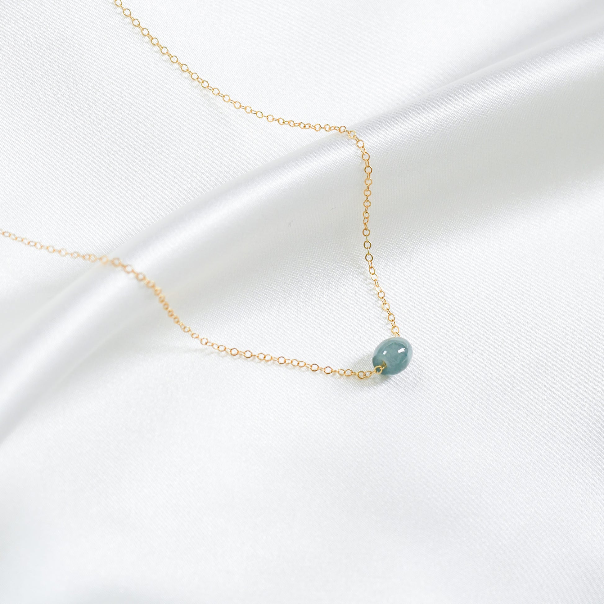 Gold necklace with a single blue jadeite barrel on a white background