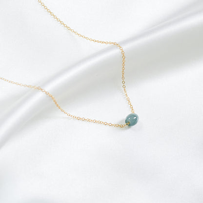 Gold necklace with a single blue jadeite barrel on a white background
