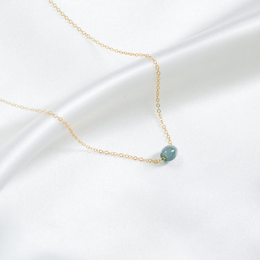 Gold necklace with a single blue jadeite barrel on a white background