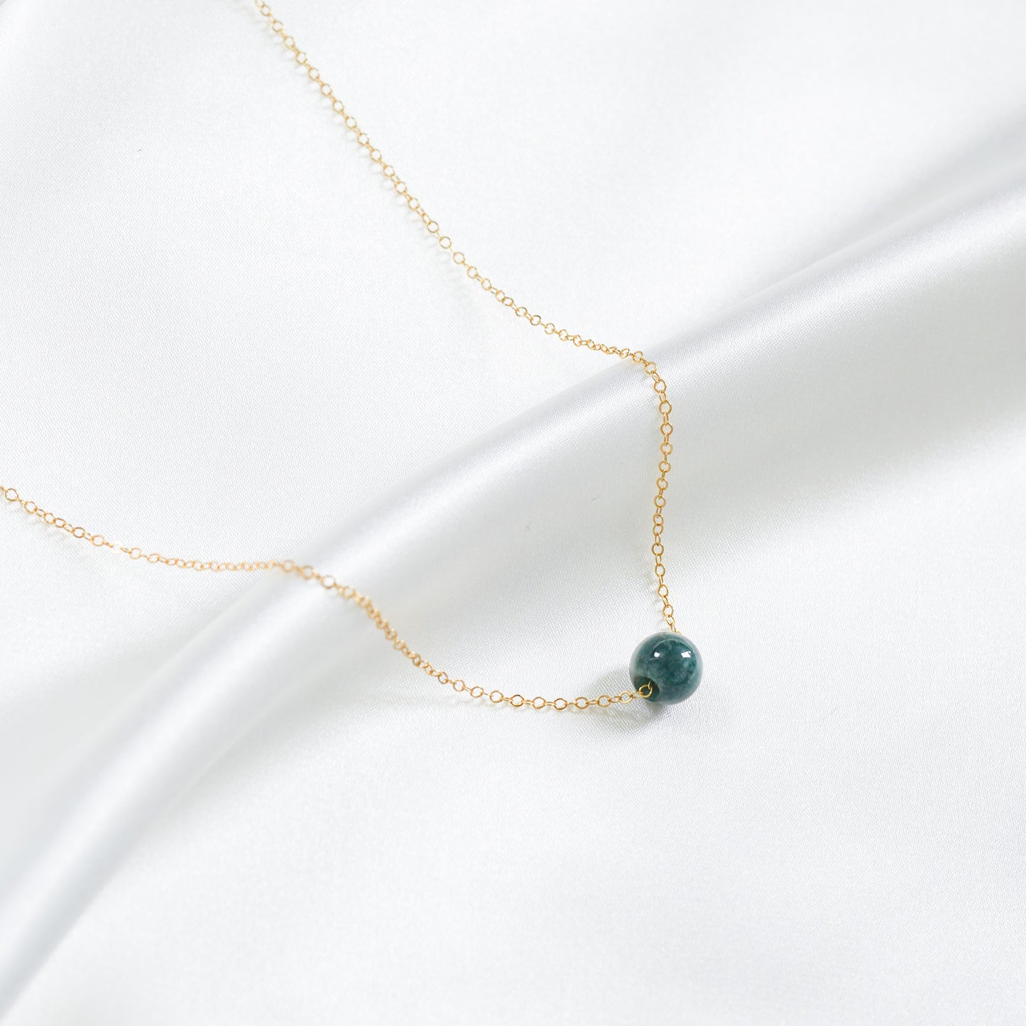 Delicate gold necklace with a green bead on a white background