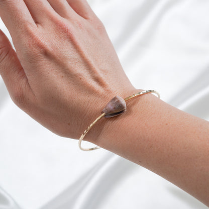 Hand wearing a gold bracelet with a shell charm on a white background