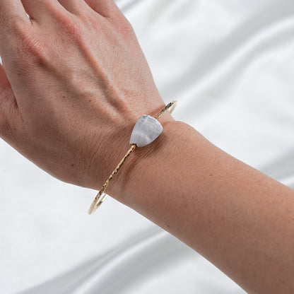 Hand wearing a gold bracelet with a white shell on a white background