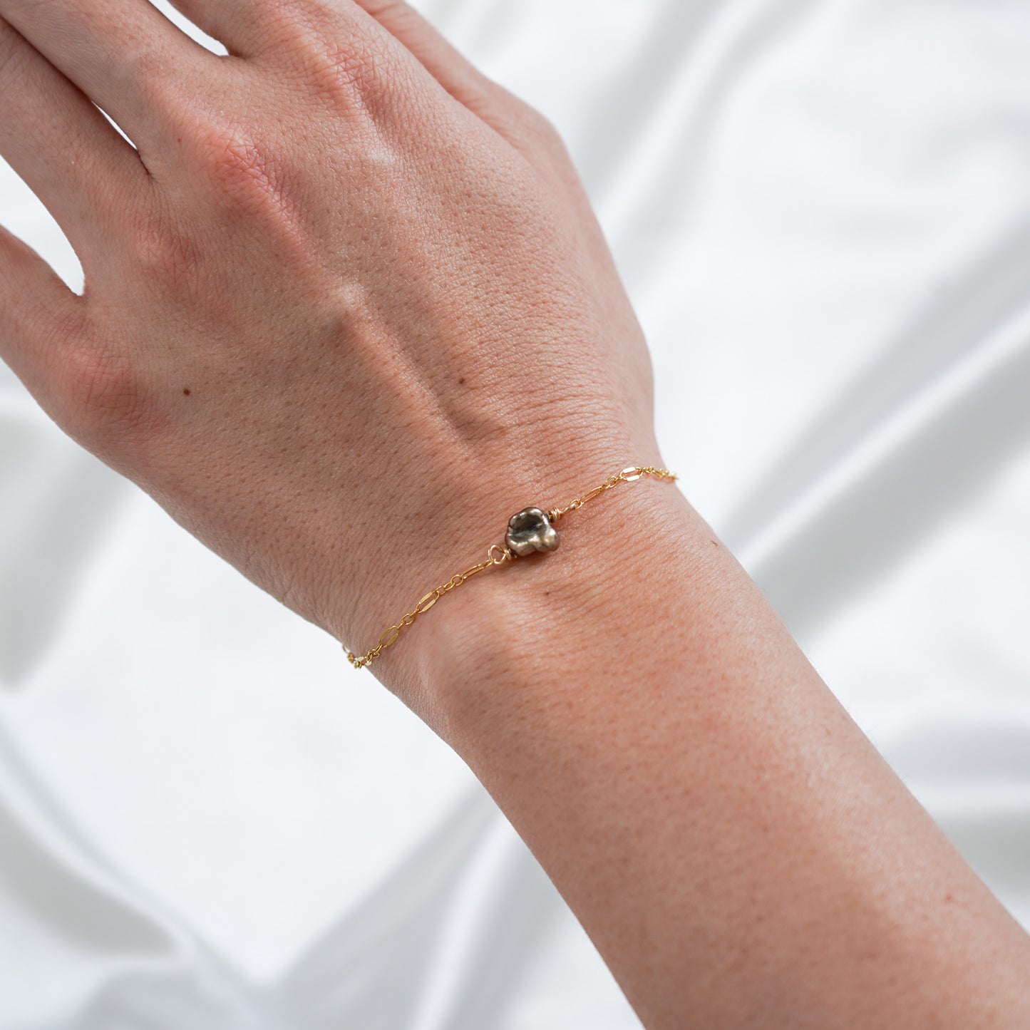Gold bracelet with a brown keshi pearl on a person's wrist against a white background