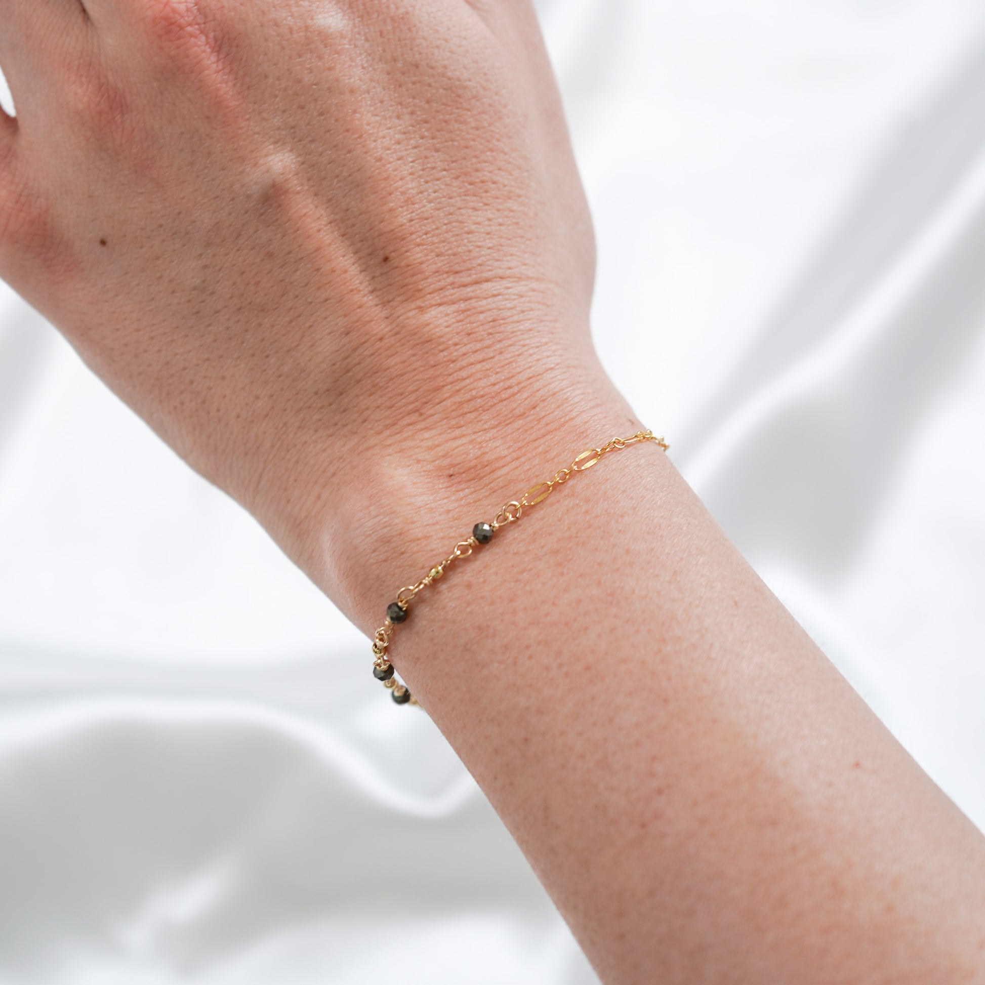 Gold necklace with black stones on a wrist against white background