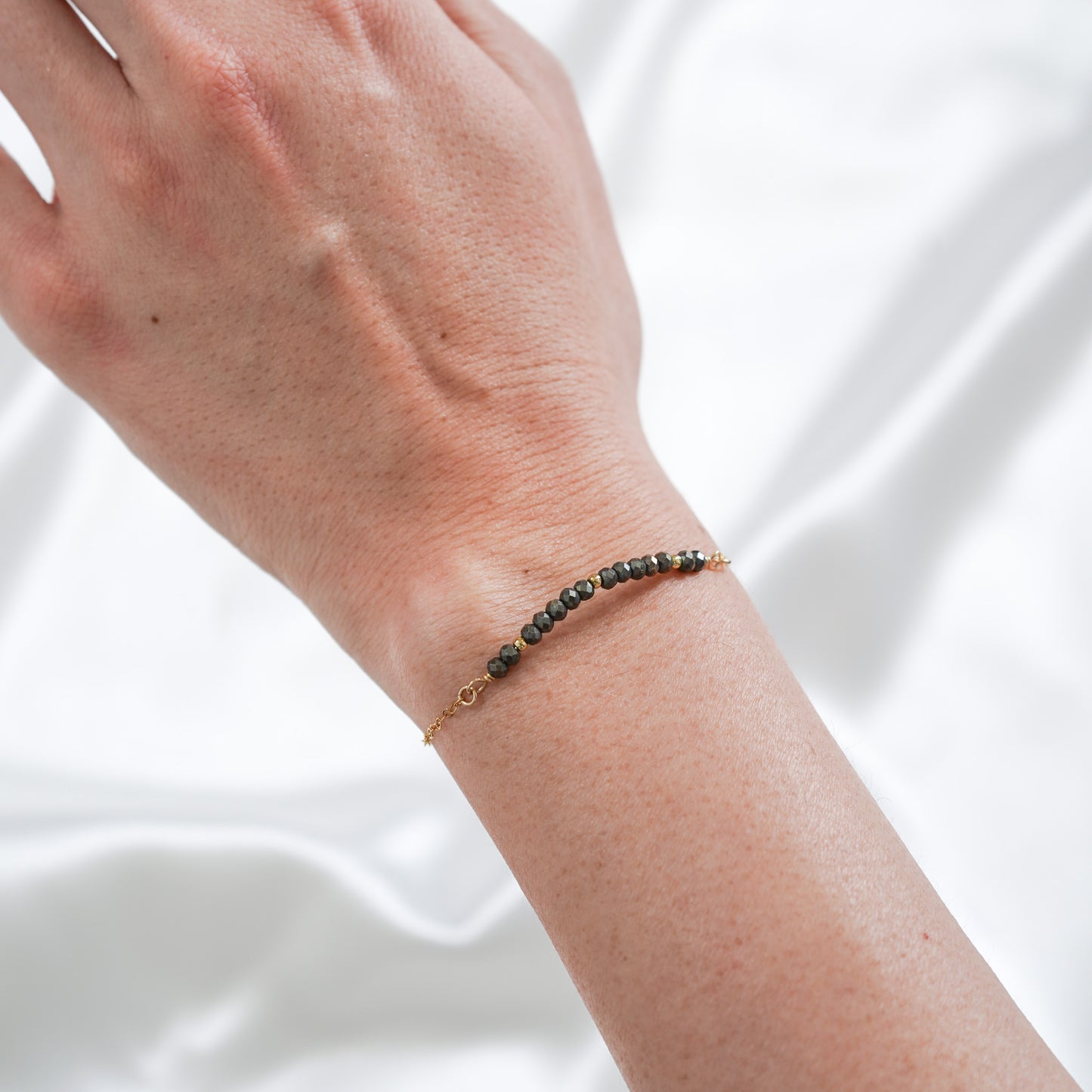 gold bracelet with black pyrite beads on wrist against white background
