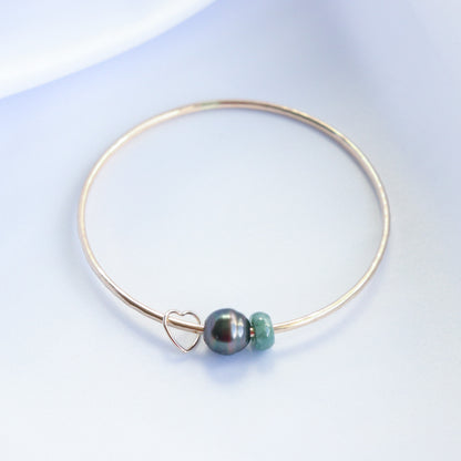 Gold bracelet with a heart charm, tahitian pearl and green jade bead on a white background