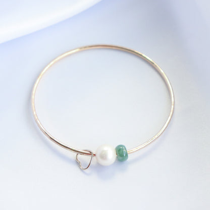 Gold bracelet with a heart charm, white pearl and green jade bead on a white background