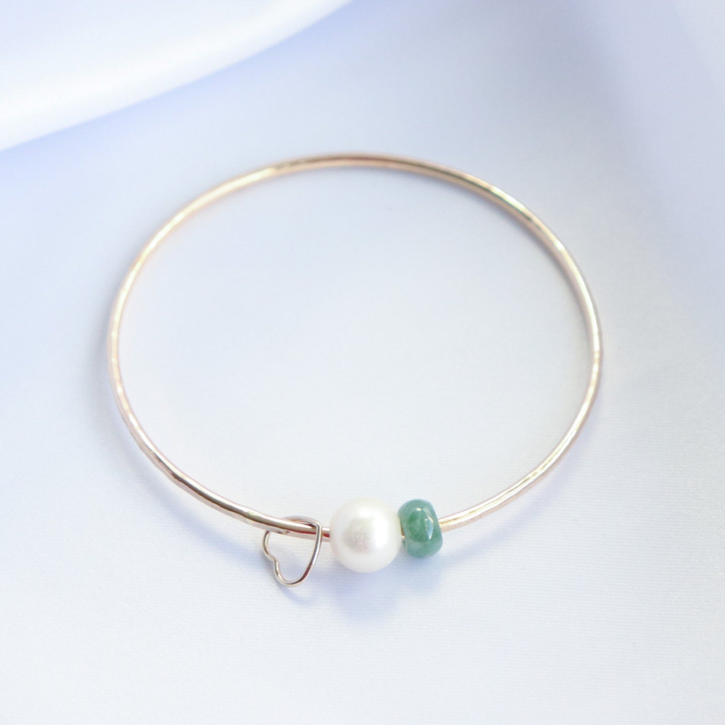Gold bracelet with a gold heart charm, white pearl and green jade bead on a white background