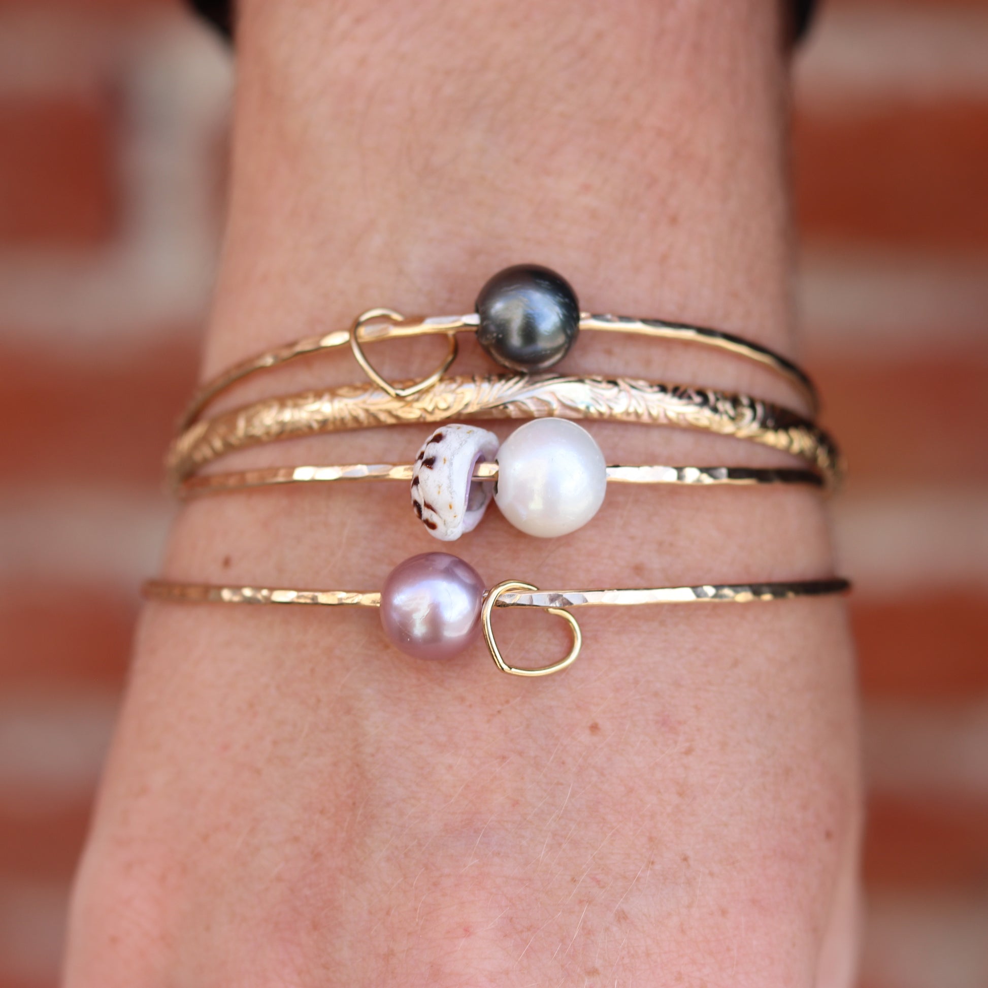 Close-up of a wrist wearing multiple gold bracelets with pearls against a blurred background