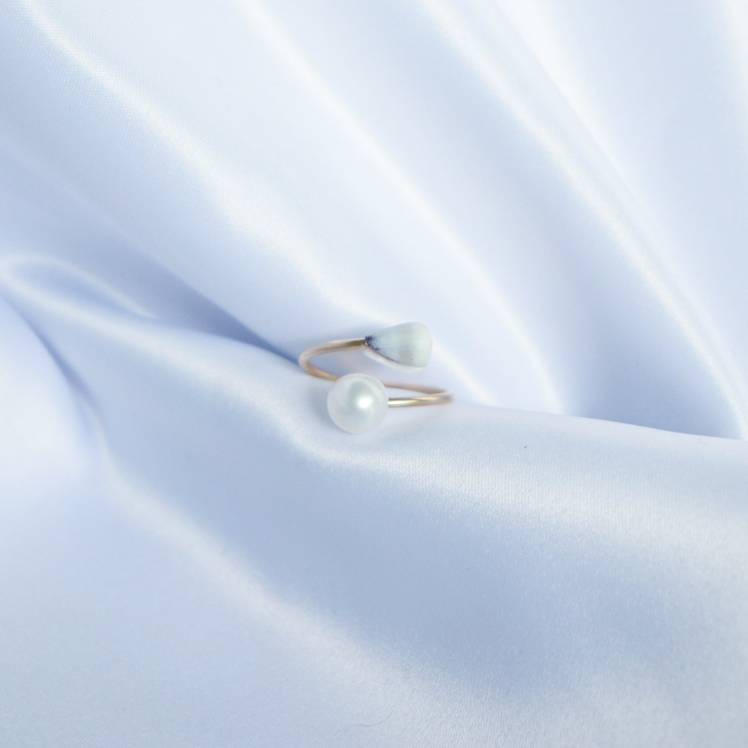 Gold ring with a tiny cone shell and white pearl on a white satin background