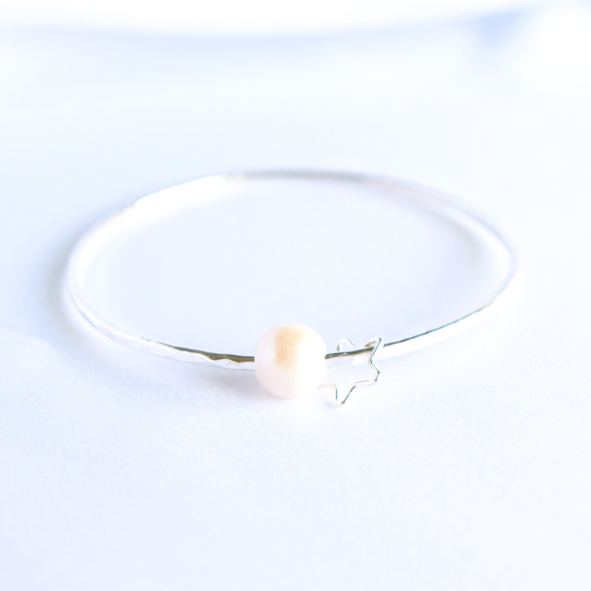Silver bracelet with a white pearl and silver star charm on a white background