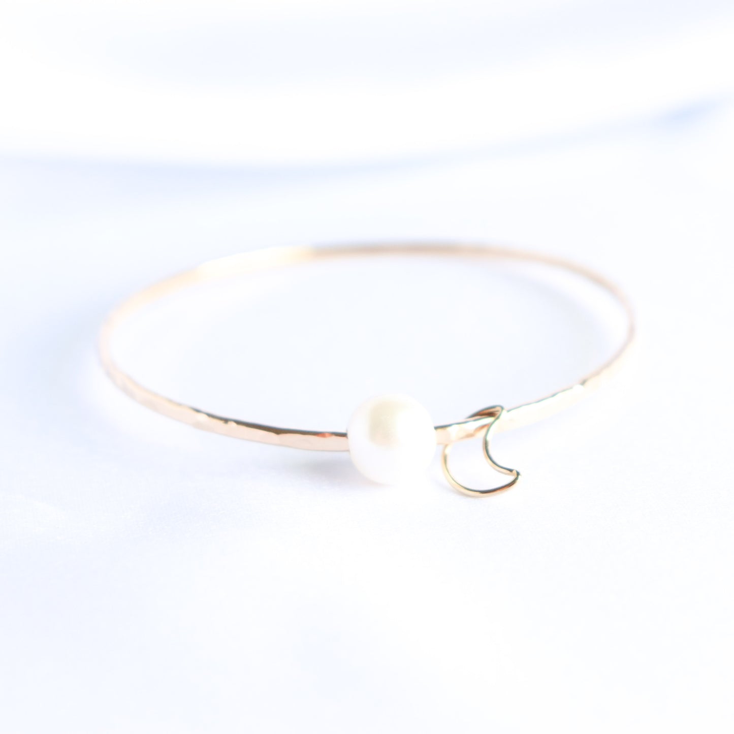 Gold bracelet with a white pearl and gold moon charm on a white background