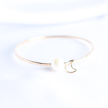 Gold bracelet with a white pearl and gold moon charm on a white background