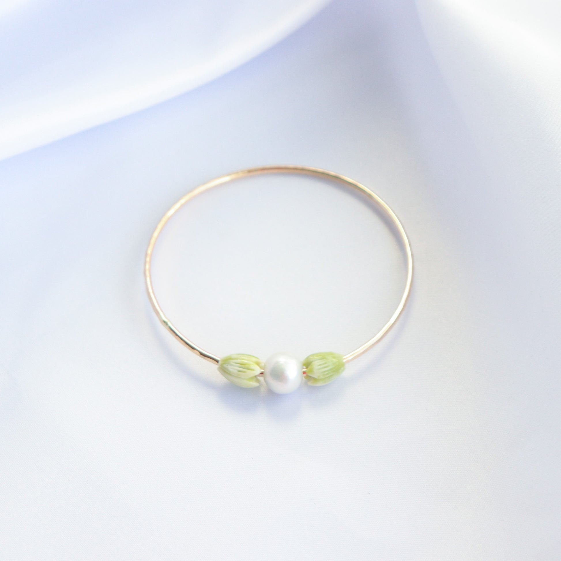 Gold bracelet with a white pearl and green pikake resin beads on either side on a white background