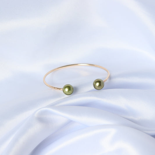 Gold bracelet with two green pearls on a white fabric background