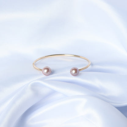 Gold bracelet with two pink pearls on a white fabric background