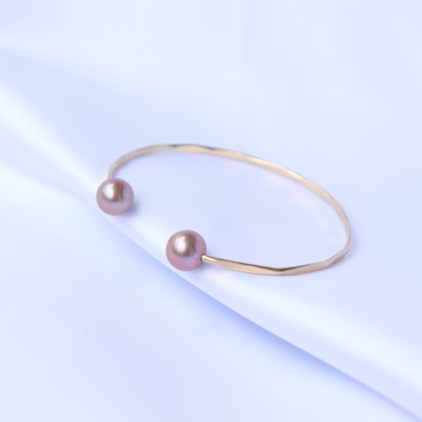 Gold bracelet with two pink pearls on a white background