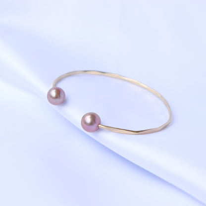 Gold bracelet with two pink pearls on a white background