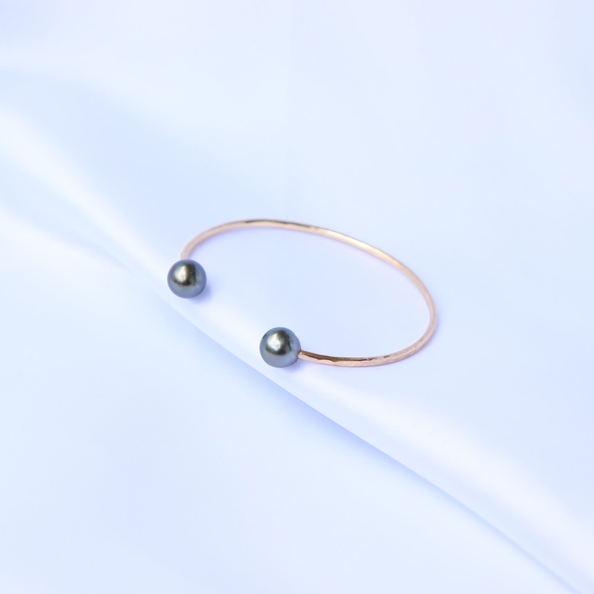 Gold bangle with two blue tahitian pearls on a white background