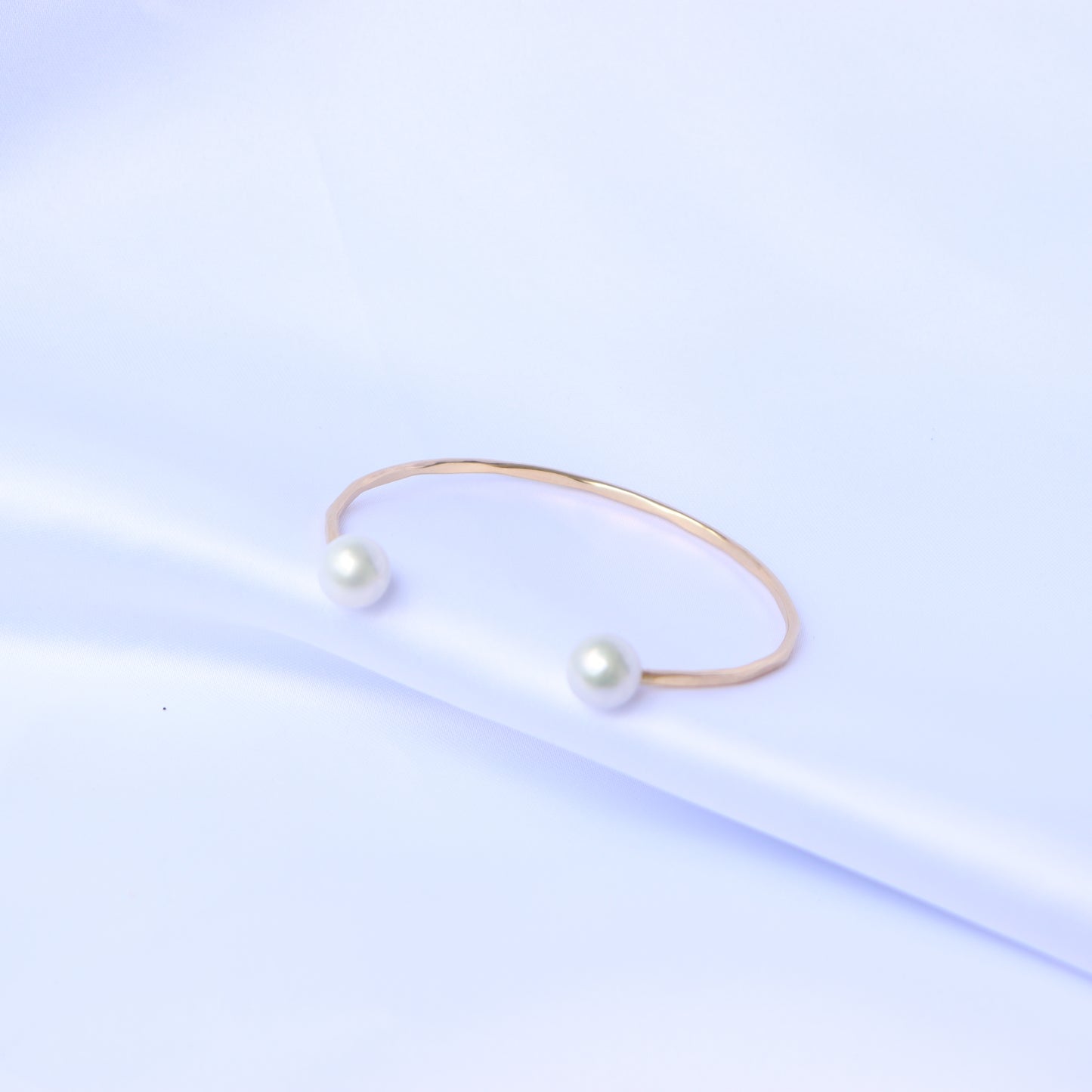 Gold bracelet with two white pearls on a white background