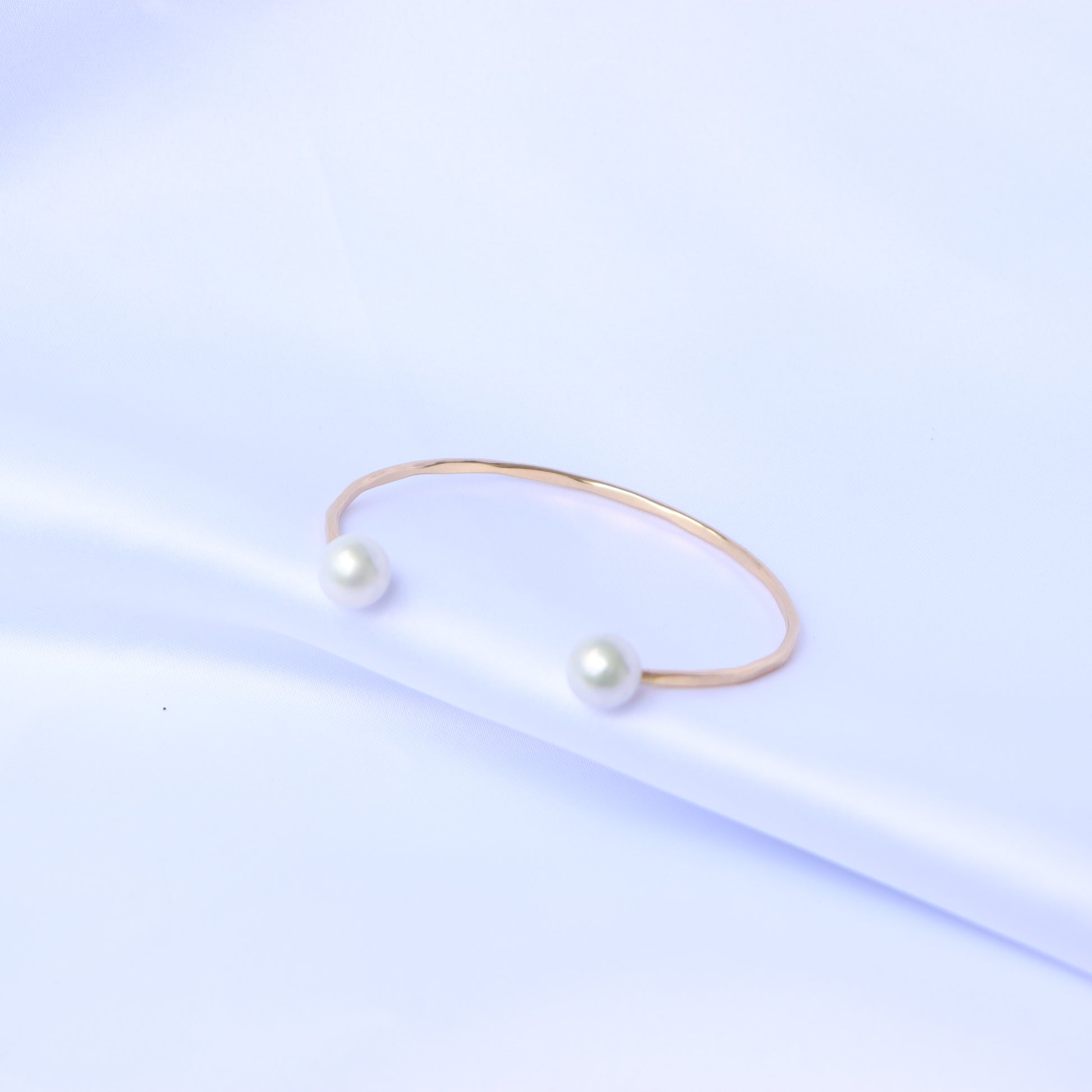 Gold bracelet with two white pearls on a white background