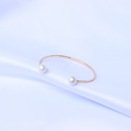 Gold bracelet with two white pearls on a white background