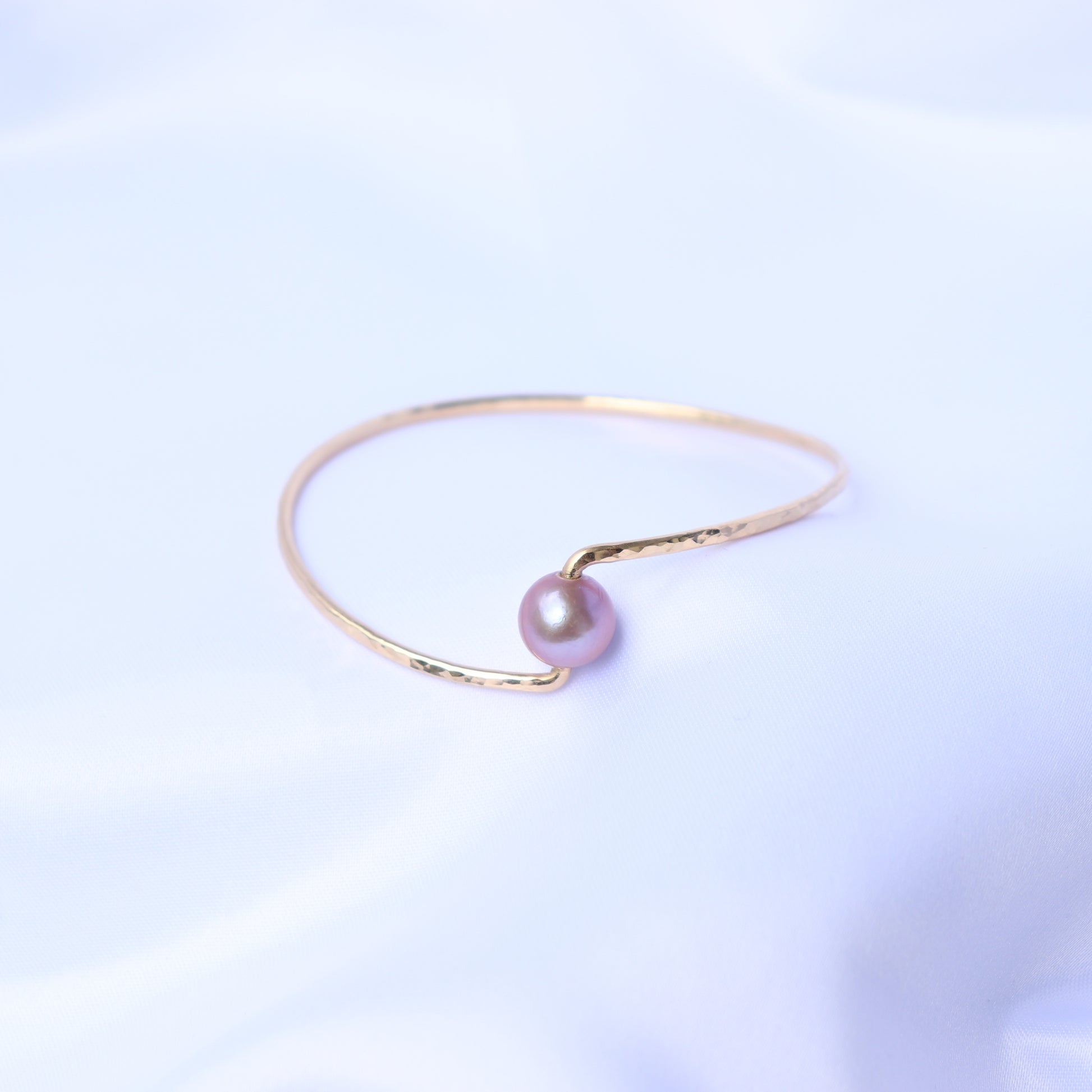 Gold bracelet with a pink pearl on a white background