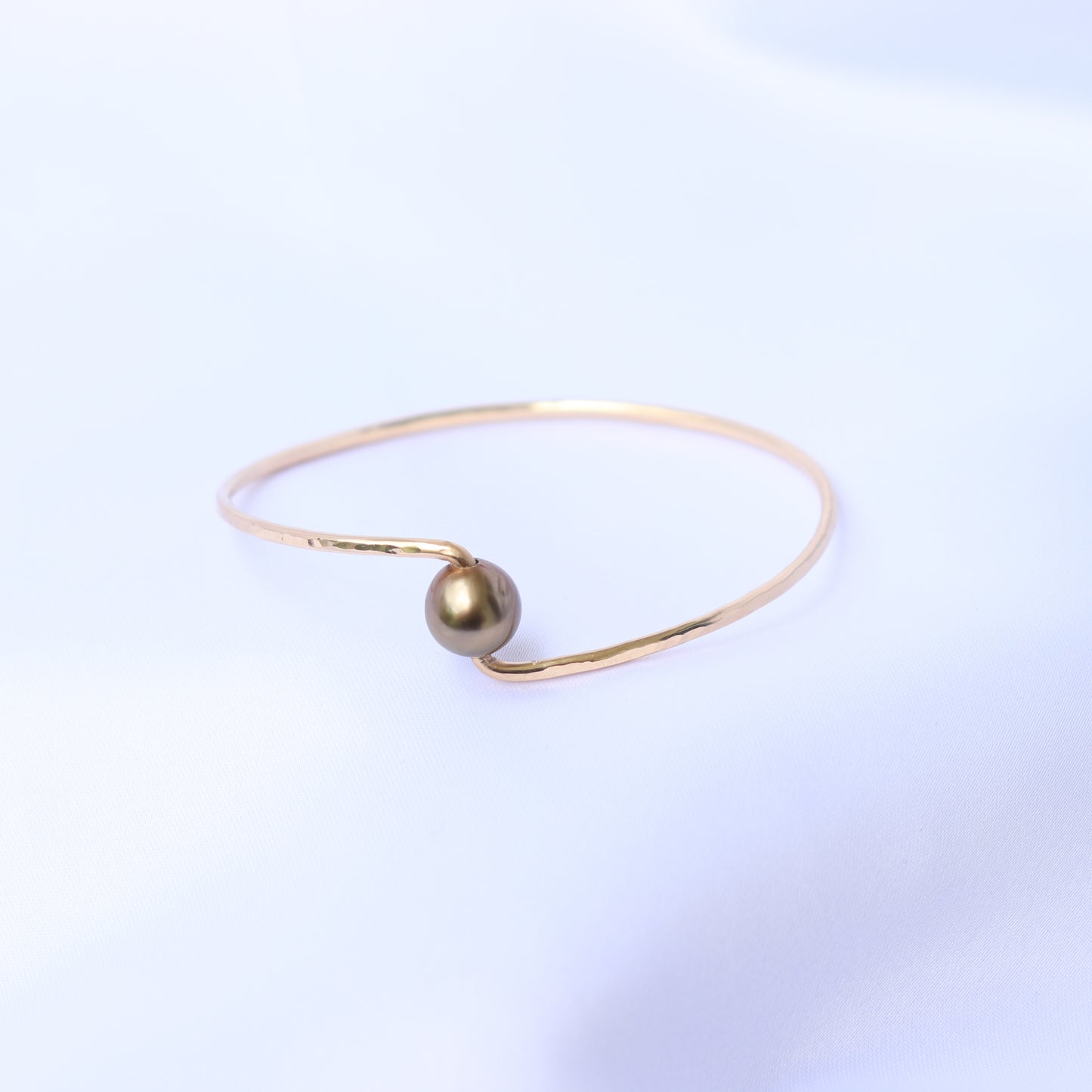 Gold bracelet with a brown pearl on a white background