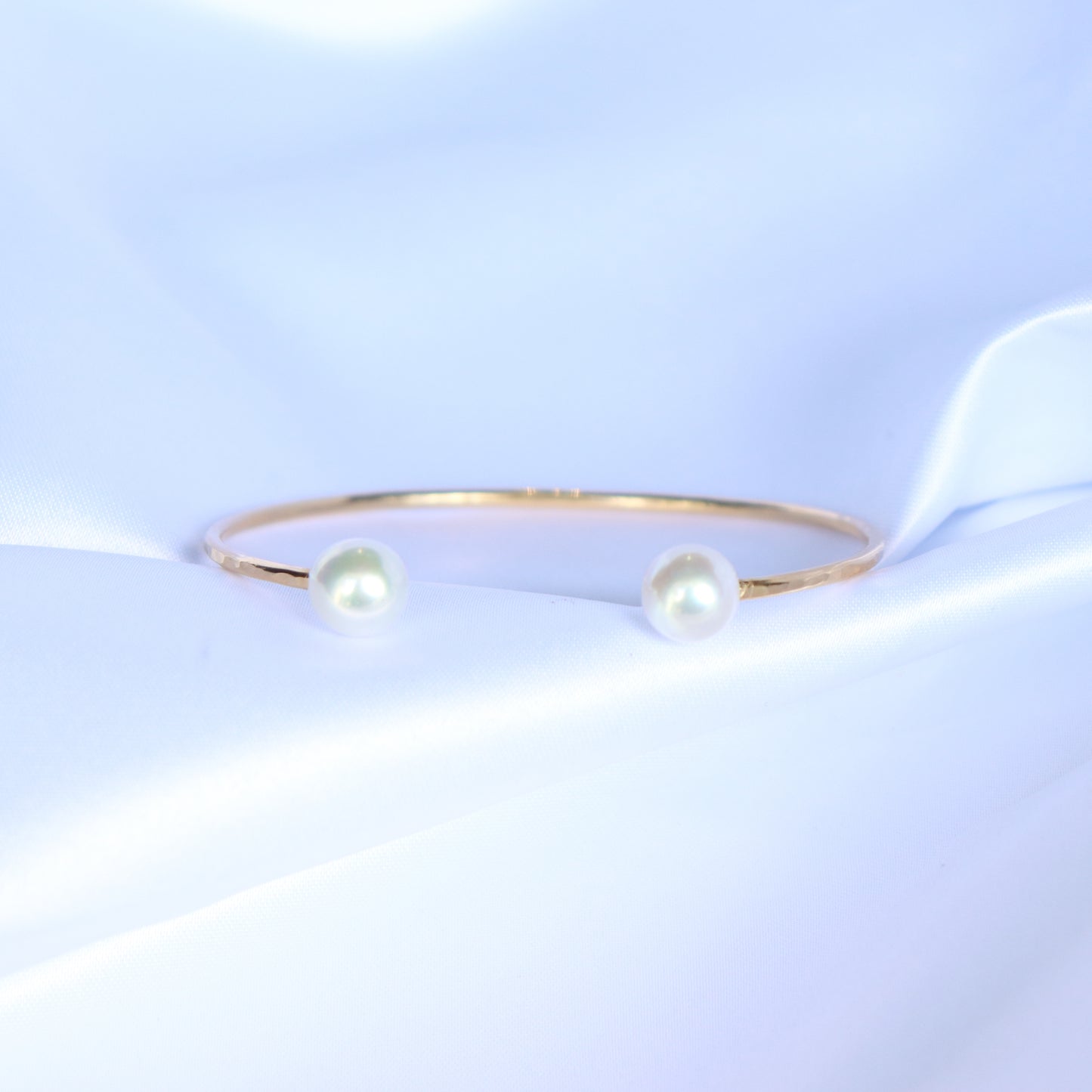 Gold bracelet with two white pearls on a white background