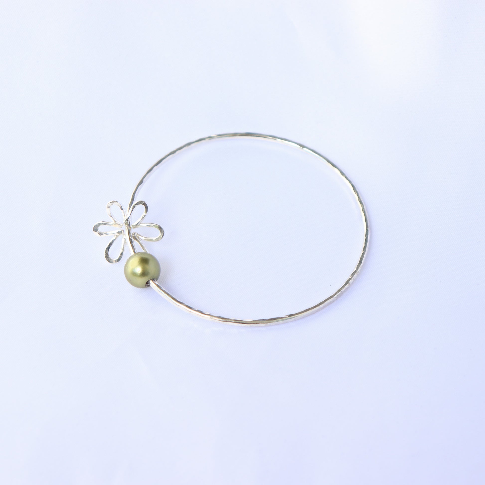 Gold bracelet with a green pearl and flower charm on a white background
