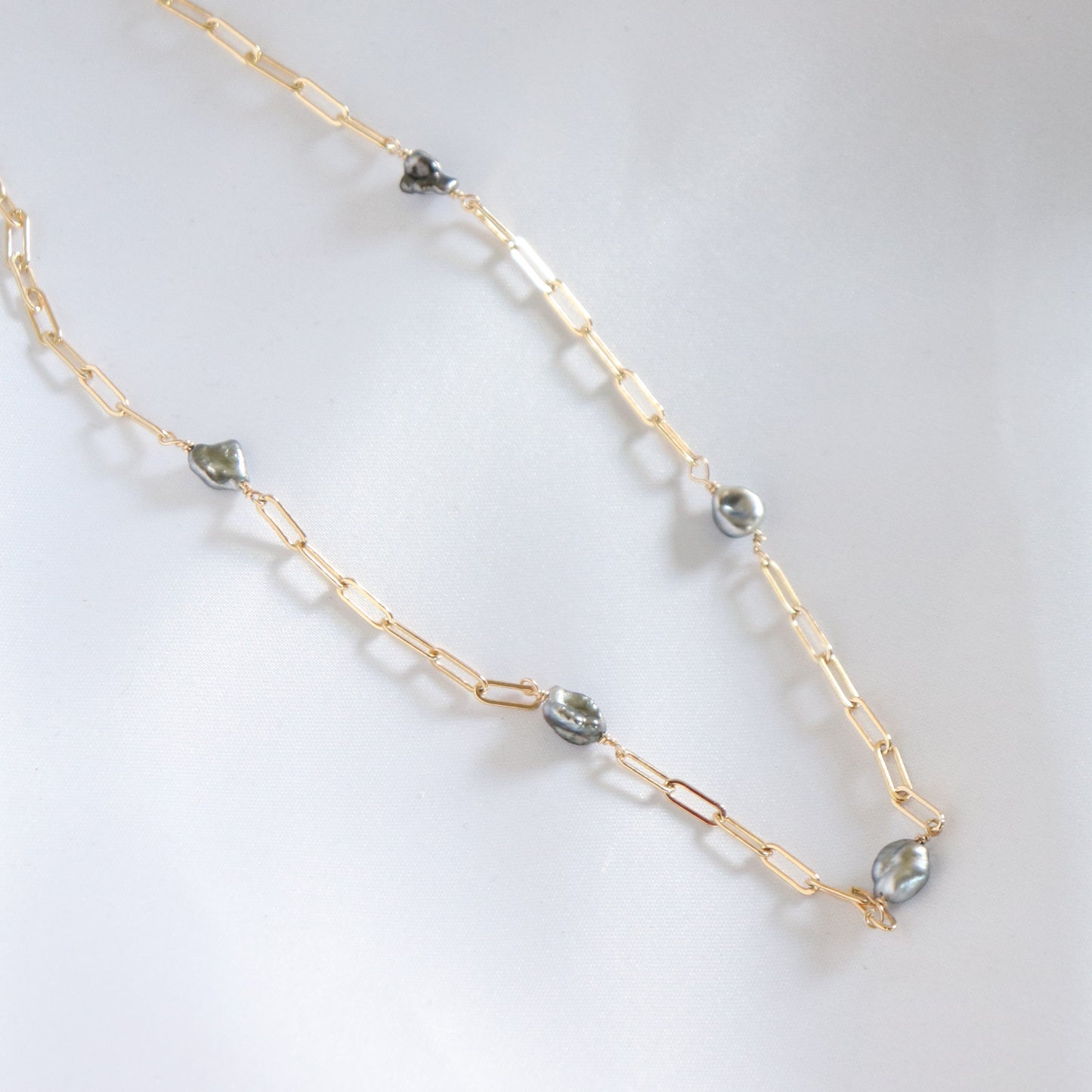 Gold chain necklace with blue keshi tahitian pearls on a white background