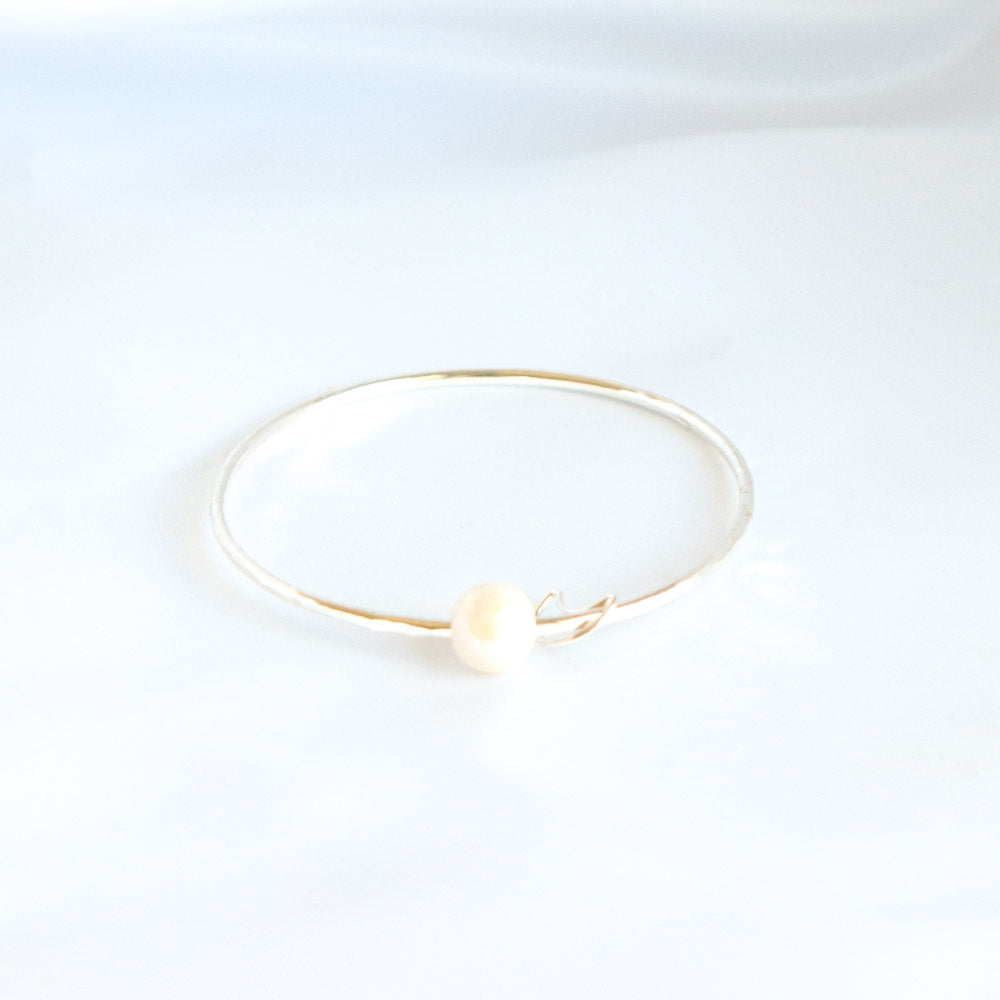 Gold bracelet with a white pearl and gold moon charm on a white background