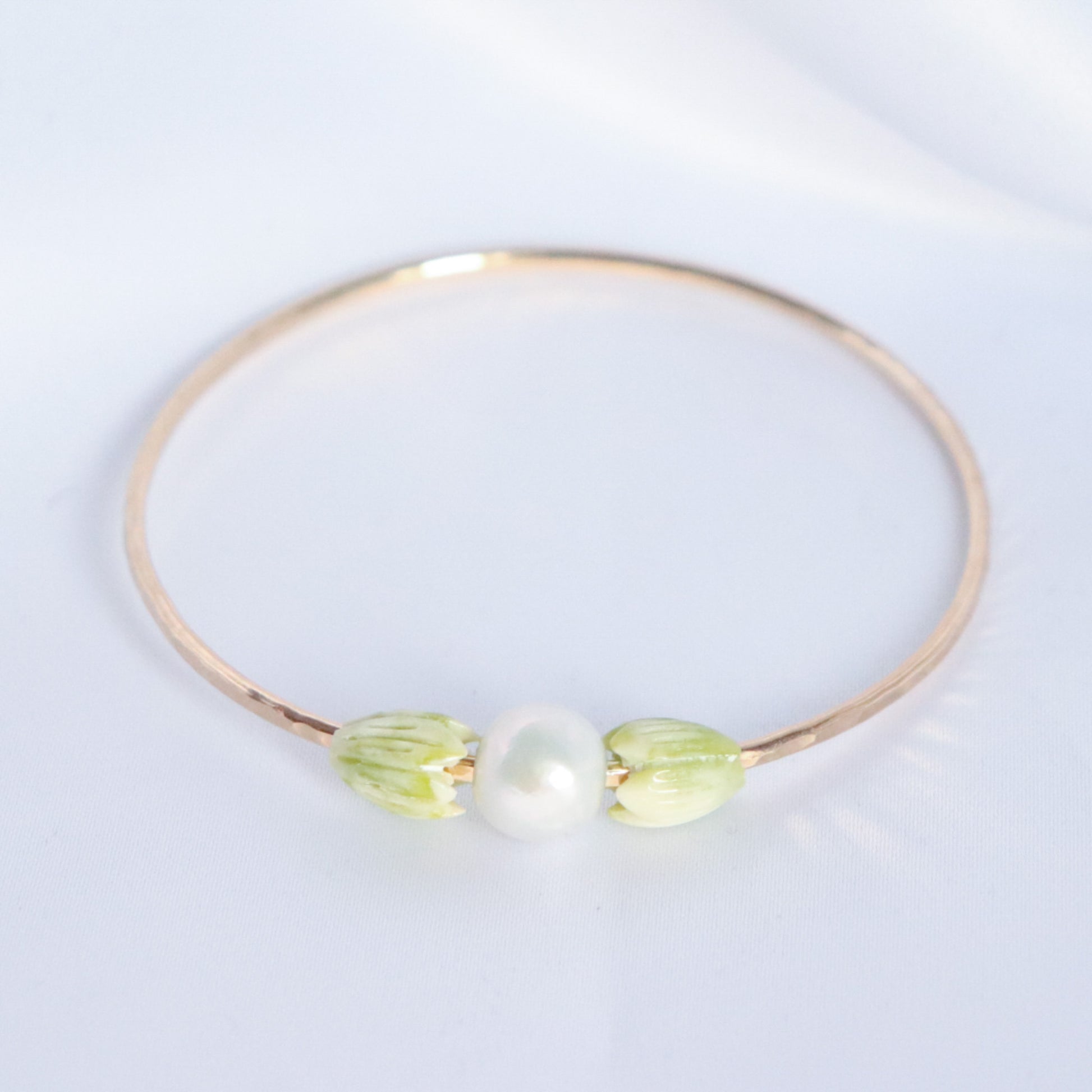 Gold bracelet with green floral elements and a pearl on a white background