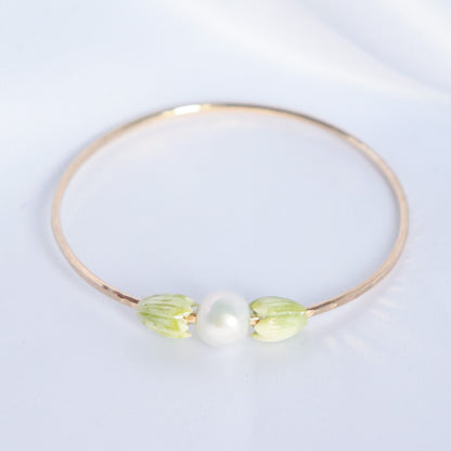 Gold bracelet with green floral elements and a pearl on a white background